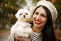 Portrait of young happy Caucasian woman in french white hat and warm coat holding and hugging her little cute white dog maltese Royalty Free Stock Photo