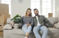 Portrait of young happy couple sitting with green flowerpot on sofa in new home. Royalty Free Stock Photo
