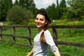 Portrait young happy hipster woman posing near wooden fence on green sunny meadow. Cheerful girl in casual wear at sprintime field Royalty Free Stock Photo