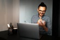 Portrait of young happy man working home at laptop, making some notes in notebook, wearing eyeglasses and shirt. Royalty Free Stock Photo