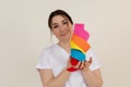 Portrait of young happy masseuse woman wearing white uniform, showing stack of kinesio tapes rolls of different colours.