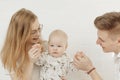 Portrait of young happy smiling beautiful family with cherubic blue-eyed infant baby toddler in white clothes sitting.