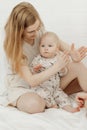 Portrait of young happy smiling beautiful mother holding cute cherubic baby toddler in white clothe playing patty-cake.