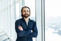 Portrait of young happy smiling business man with crossed hands standing near panoramic window Royalty Free Stock Photo