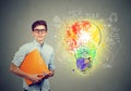 Portrait of young happy smiling man with orange folder notebook near a concrete wall with a bright light bulb business idea sketch