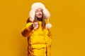 Portrait of young, happy, smiling man in winter warm coat and fur hat posing against yellow studio background Royalty Free Stock Photo