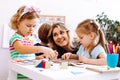 Portrait of young happy woman sitting at table with colored pencils board games. Teacher looking at serious little girl. Royalty Free Stock Photo