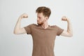 Portrait of young healthy sportive man looking at his biceps muscles boasting over white background.