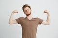 Portrait of young healthy sportive man showing biceps muscles boasting looking at camera over white background.