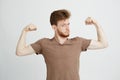 Portrait of young healthy sportive man showing biceps muscles boasting looking at camera over white background.