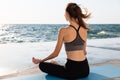 Portrait of young healthy woman sitting in lotos pose while practicing meditation at seaside