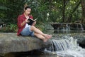 Portrait of young hipster man in red shirt reading a book in beautiful nature background.