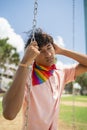 portrait of young hispanic gay boy sitting on swing with eyes closed, wearing pink polo shirt - vertical image Royalty Free Stock Photo