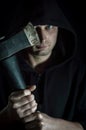 Portrait of a young hooded man with blue eyes who with an ax in his hand has a disturbing look - focus on the blade