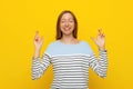 Portrait of young hopeful woman cross fingers, making wish, hoping for smth, wishing, standing over yellow background with Royalty Free Stock Photo