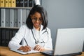 Portrait of young indian doctor working in the hospital while looking at laptop and write on clipboard. Royalty Free Stock Photo