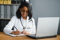 Portrait of young indian doctor working in the hospital while looking at laptop and write on clipboard. Royalty Free Stock Photo