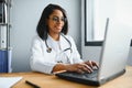 Portrait of young indian doctor working in the hospital while looking at laptop and write on clipboard. Royalty Free Stock Photo