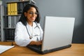 Portrait of young indian doctor working in the hospital while looking at laptop and write on clipboard. Royalty Free Stock Photo