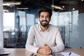 Portrait of a young Indian man in a shirt sitting smiling at a desk in the office and looking confidently at the camera Royalty Free Stock Photo