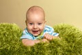 Portrait of young innocent smiling baby. Small boy lies on knitted green plaid like a grass. Positive