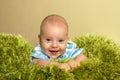 Portrait of young innocent smiling baby. Small boy lies on knitted green plaid like a grass. Positive