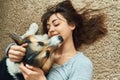 Portrait young joyful woman lying on carpet with cute pet. Happy girl playing and stroking Welsh Corgi dog. Royalty Free Stock Photo