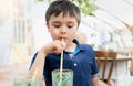 Portrait Young kid drinking fresh juice for breakfast in cafe,Happy child boy drinking glass of soda or soft cold drink while Royalty Free Stock Photo