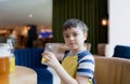 Portrait Young kid drinking fresh orange juice for breakfast in cafe, Happy child boy holding glass of fruit juice while waiting Royalty Free Stock Photo