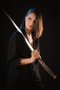 Portrait of a young kung fu brunette girl in a kimono with a Japanese sword on a black background Royalty Free Stock Photo