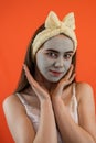 Portrait of young lady with green nourishing caly mask on face isolated on orange