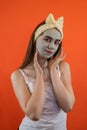 Portrait of young lady with green nourishing caly mask on face isolated on orange