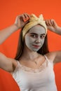Portrait of young lady with green nourishing caly mask on face on orange