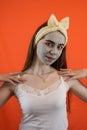 Portrait of young lady with green nourishing caly mask on face on orange