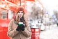 Portrait of a young lady in warm clothes and headphones, standing on the background of the street, paper cup of coffee in her Royalty Free Stock Photo