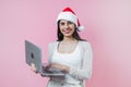 Portrait of young latin woman holding a computer with copy space in a christmas concept on pink background Royalty Free Stock Photo