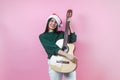 Portrait of young latin woman holding guitar music with copy space in a christmas concept on pink background Royalty Free Stock Photo