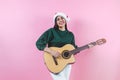 Portrait of young latin woman holding guitar music with copy space in a christmas concept on pink background Royalty Free Stock Photo