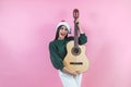 Portrait of young latin woman holding guitar music with copy space in a christmas concept on pink background Royalty Free Stock Photo