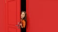 Portrait of young little girl, kid peeking out red door and attentively looking, overhearing. Playful and curious mood Royalty Free Stock Photo