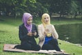 Portrait of young lovely pleasant mix ethnic woman sitting on grass at summer green park and having a discussion