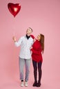 Portrait of young loving, beautiful couple, man and woman holding balloon in heart shape against pink studio Royalty Free Stock Photo