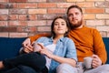 Portrait of young loving couple hugging, holding cups of warm drink and watching romantic movie on TV at evening Royalty Free Stock Photo