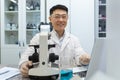 Portrait of young male Asian student, intern studying and working in laboratory with microscope and laptop. Sitting at Royalty Free Stock Photo