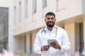 Portrait of a young male doctor, nurse, standing outside the hospital, holding a tablet and looking into the camera Royalty Free Stock Photo