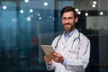 Portrait of a young male doctor standing in an office in a hospital, holding a tablet in his hands Royalty Free Stock Photo