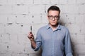 Portrait of young male hairdresser in glasses, posing with scissors, on gray brick wall background, front view Royalty Free Stock Photo