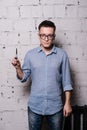 Portrait of young male hairdresser in glasses, posing with scissors, on gray brick wall background, front view, vertical Royalty Free Stock Photo