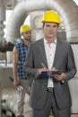 Portrait of young male manager writing on clipboard with manual worker in background at industry