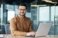 Portrait of a young male office worker, businessman smiling and posing at the camera and working on a laptop while Royalty Free Stock Photo